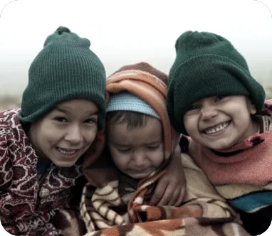 Three smiling kids in knit hats huddled together